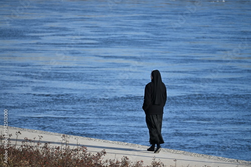 Nun Walking Along Riverside Promenade Seen From Behind
