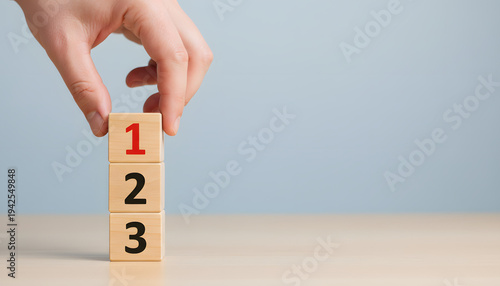Photos A human hand carefully places the number one wooden block on top of a stack of n