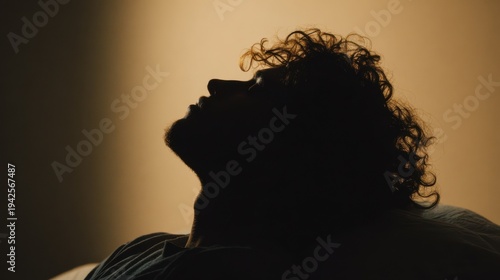 A silhouette of a man looking upwards, bathed in warm light. His features are softly defined, with his eyes closed in a moment of reflection