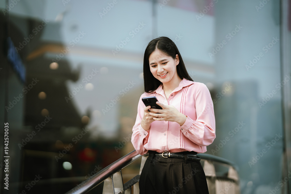 Fototapeta premium Smiling young woman talking on a smartphone outdoors in an urban area, expressing friendly communication, mobile connectivity, and modern digital lifestyle.