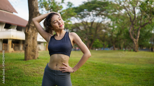 Confident woman resting after training with hands behind her back, breathing deeply and enjoying fresh air in a sunny park. Mindfulness and self care concept.