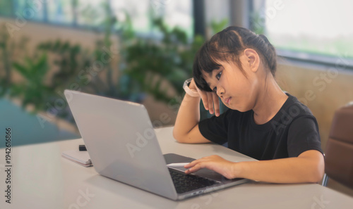 Tired child using laptop for online learning, fatigue and screen time concept at home or cafe.
