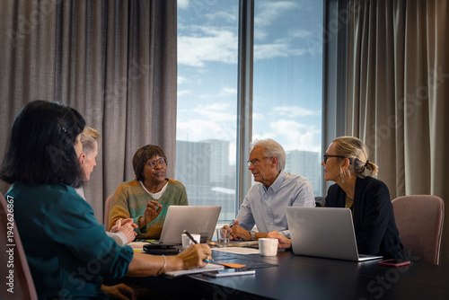 Mature female business professional explaining strategy to colleagues while sitting in office board room