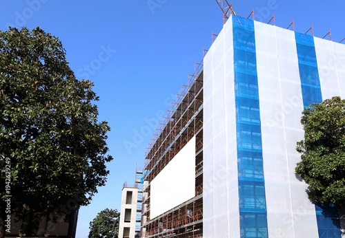 Wallpaper Mural Facade of  building under construction with plastic sheet covering on the right and  blank information board on the left. Background for copy space and add text. Torontodigital.ca
