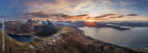 Aerial view of majestic mountains with snow-dusted peaks meet the tranquil fjords under a fiery sunset, Senjahopen, Troms, Norway.