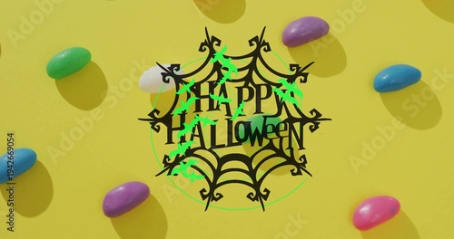 Showing central black spiderweb saying HAPPY HALLOWEEN on yellow table with neon bats, jellybeans
