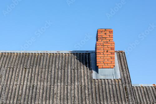 Brick Chimney on Old Asbestos Cement Roof Against Clear Blue Sky