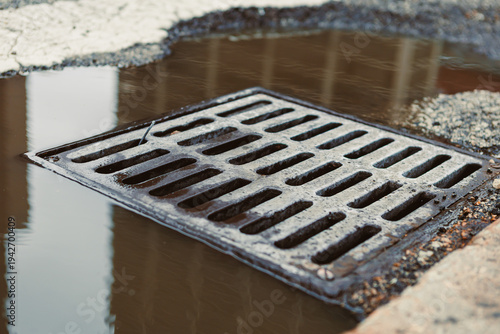 Drain cover sits near a puddle on a city road after rain during the day
