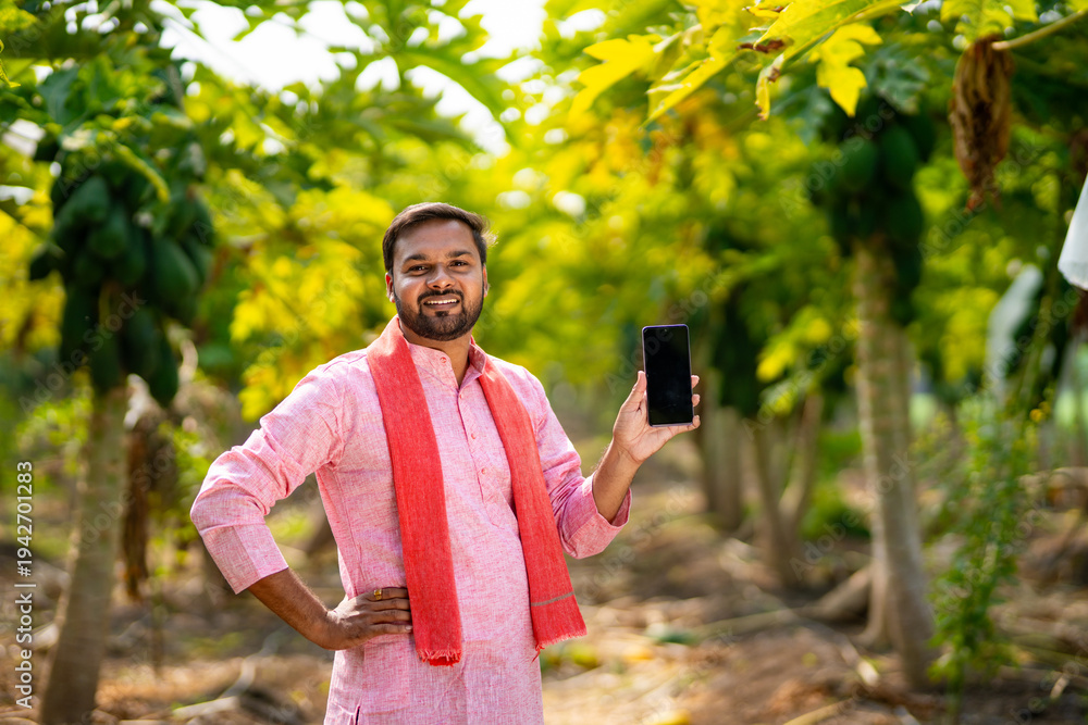 Fototapeta premium young indian farmer using smartphone standing at papaya field