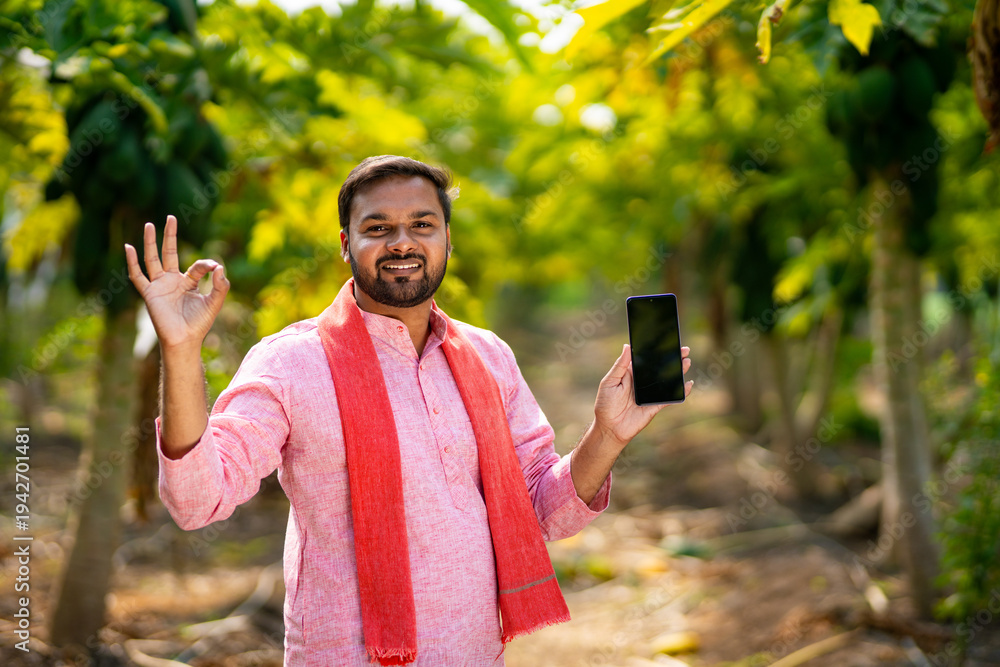 Fototapeta premium young indian farmer using smartphone standing at papaya field