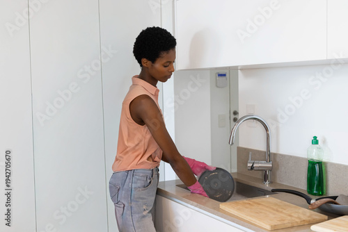 Mid-adult African American woman washing frying pan at kitchen sink wearing pink rubber gloves