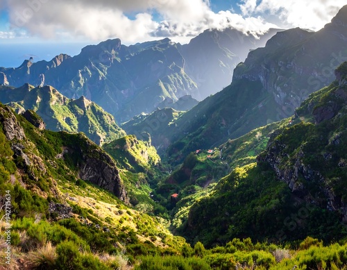 A scenic mountainous landscape captures sunlit peaks, verdant valleys, and dramatic cloud formations near the ocean