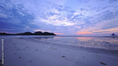 Curved low tide shoreline beneath blue crepuscular sky in Thailand