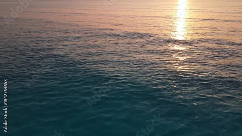 Serene ocean waves gently ripple under the warm glow of the setting sun, creating a tranquil scene of water and light reflecting on the surface