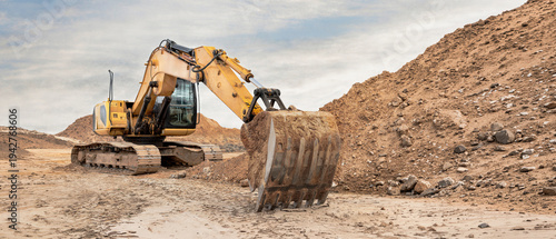 Heavy machinery moves soil and rocks at a construction site. The excavator digs into the ground while piles of dirt surround the area during the day