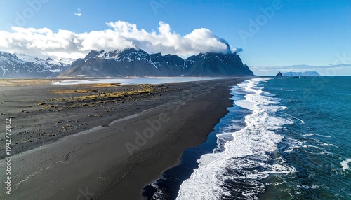 Scenic coastal view of a black sand beach and mountains under a blue sky