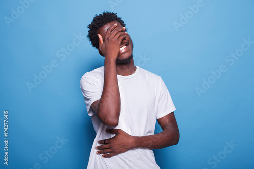 Принти на полотні Uplifting and joyous after hearing amusing joke, African American man with afro hair bursts into laughter while placing his hands on his eyes and stomach