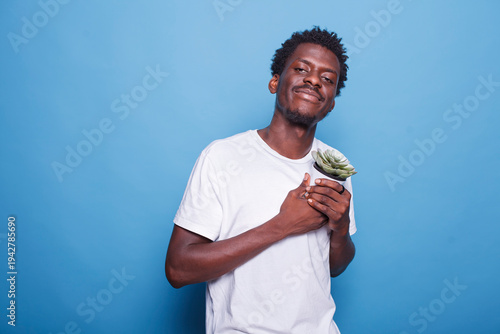 Portrait of black guy carrying container with plants for their botany hobby. Cheerful african american man holding dearly a flowerpot with green leaves for gardening concept and ecology.