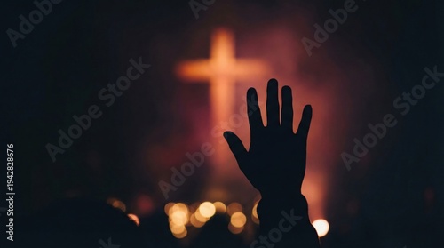 Silhouette of woman hand raised during christian worship service directed at glowing cross. Religious community prayer during easter and palm sunday. Spirituality and faith in church.