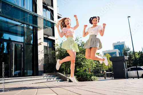 Playful young friends jump in the city sunshine as stylish travelers enjoy urban lifestyle and summer fashion in a vibrant carefree moment in the streets of 
