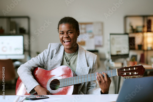 Fotografie Portrait of young adult Black woman smiling while playing acoustic guitar at des