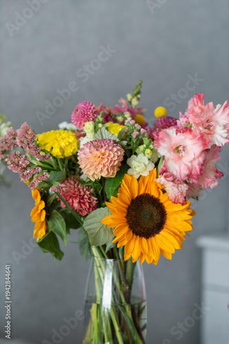 Vibrant mixed flower bouquet in glass vase with sunflower and dahlias