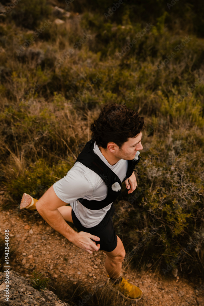 Fototapeta premium High angle view of a trail runner running along a narrow dirt path through rugged mountain terrain. Outdoor adventure fitness and endurance sport in natural wilderness