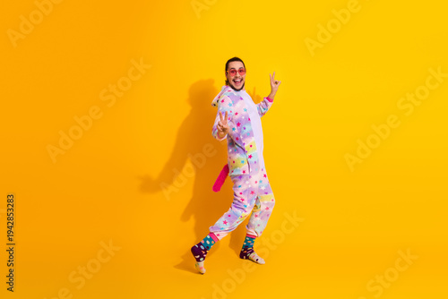 Canvas Print Happy man in colorful unicorn pajama jumpsuit poses on yellow background