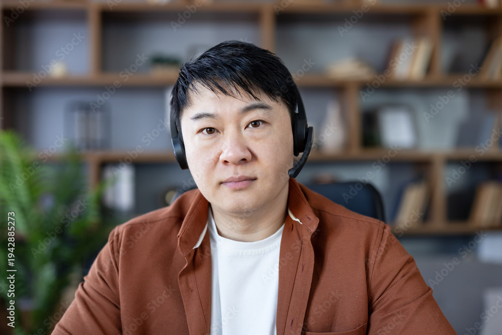Fototapeta premium Man in headset looking directly at camera, having a video conference call from home office, representing remote work, technical support, or online communication