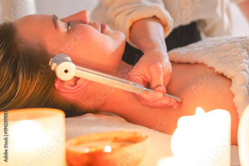 Konstfotografi Tuning fork sound therapy with candles, practitioner applying vibration to woman's neck, holistic wellness ritual, relaxation, alternative spa treatment, close up