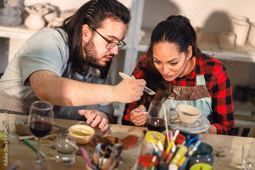 Man and woman focused on sculpting clay bowl together in pottery workshop.