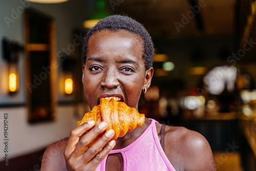 Playful Black woman biting croissant in close up cafe portrait