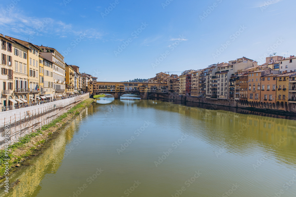 Obraz premium Ponte Vecchio bridge spanning Arno river in Florence, Italy, with historic buildings lining the banks