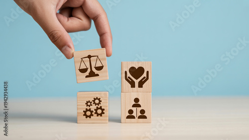Hand placing a block with a scales of justice icon onto a tower of wooden cubes.