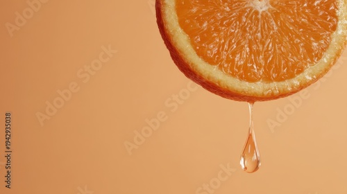 Close-up of fresh orange half dripping juice with single droplet on warm peach background
