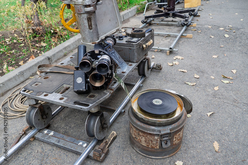 Vintage motion picture film camera mounted on dolly cart with rails and open film reel on a movie set. Retro analog cinematography equipment used in traditional filmmaking and film production.
