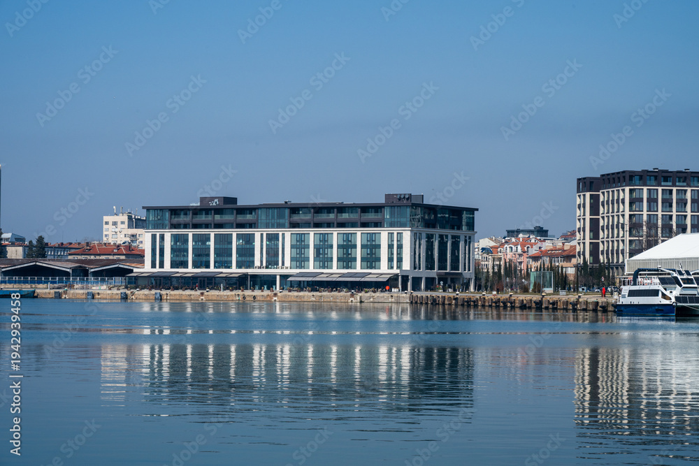 Obraz premium a modern white hotel or commercial building located on a waterfront pier, reflecting in the calm, still water under a clear blue sky.