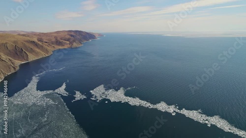 Aerial view of the blue expanse of Lake Baikal with ice floes. Ice drift. Beautiful mountain landscape from the air.