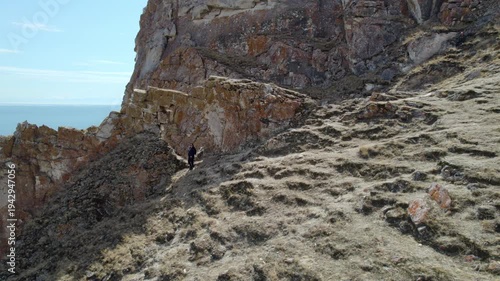 A female hiker stands at an arch in a cliff with a picturesque view of Lake Baikal. A beautiful spring landscape. Ice melt period. Hiking. Aerial shot.
