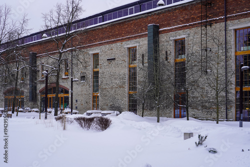 Snow covers a park area in front of a large brick building during winter in a city with clear skies and a chill in the air