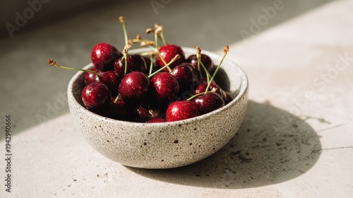 Freshly picked cherries in a rustic bowl placed on a light stone surface with natural sunlight creating soft shadows and enhancing vibrant colors of fruit