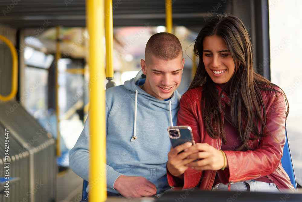 Obraz premium Young couple enjoying time together while using smartphone on a bus in an urban setting during the day