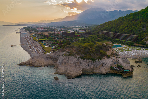 Aerial drone view of luxury beach resort on Mediterranean coastline with mountains at sunset