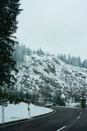 Winter road winding through snow-covered mountains under a gray sky, inviting adventure and exploration in a serene, tranquil landscape