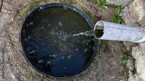 Water flowing from pipe into ground container creating bubbles and ripples
