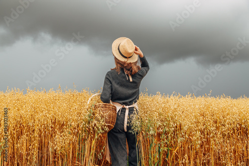 Girl in a wheat field wearing a straw hat on a cloudy day. Back view