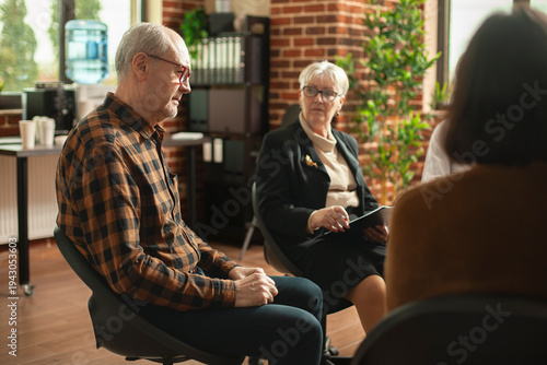 Photos Sad male pensioner sitting and talking about his mental health during aa group meeting as retired female therapist is taking notes
