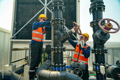 Tablou pe pânză Two male technicians in safety vests and hard hats inspect large industrial pipe