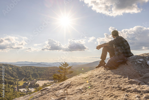 African American man sitting on a rock outcropping after a hike in nature and wilderness taking in a stunning view, Vermont, New England, USA. Thrill and exercise at the top of a mountain.