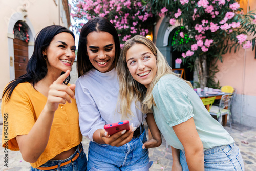 Foto Multiracial young female friends looking at smartphone outdoors
